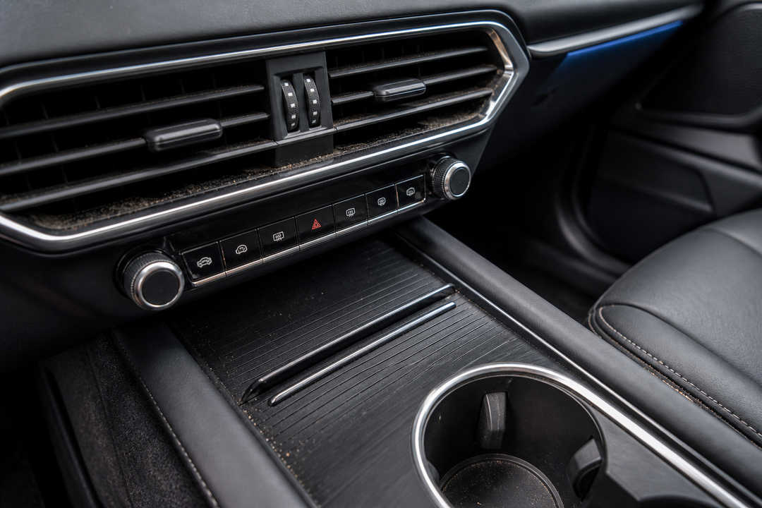 Vehicle interior tight spaces requiring detailed cleaning  Modern vehicle dashboard and center console with dust concentrated in air vent slats, button gaps, trim seams and a cup holder.